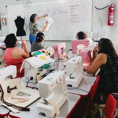 Aula de costura com alunas e professora explicando padrões.