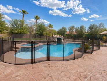 Black removable mesh pool safety fence with a locking gate surrounding a curved pool, raised spa, an