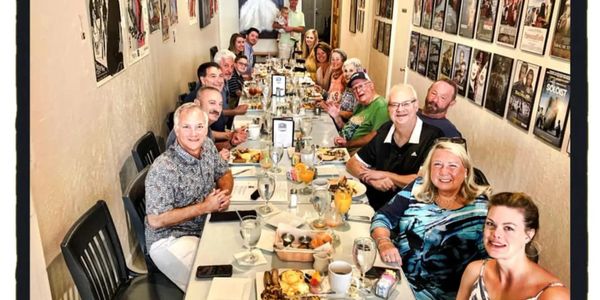Large group enjoying a meal together in a cozy, art-filled room.