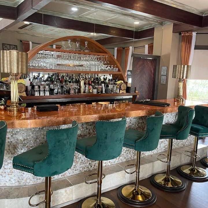 Elegant bar with green velvet stools and a wooden countertop.
