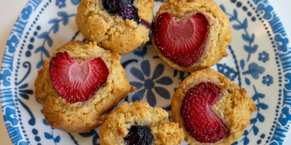 Homemade muffins with fresh strawberries and blueberries on a patterned plate.