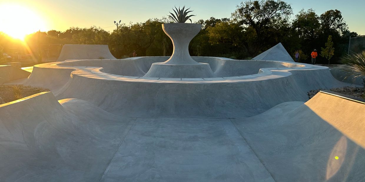 Empty concrete skatepark with a large planter centerpiece at sunset.