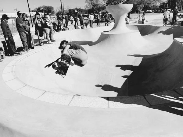 Skateboarder performing a trick in a skate bowl surrounded by onlookers.