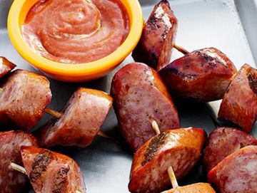 Grilled sausage chunks served with a bowl of dipping sauce on a tray.