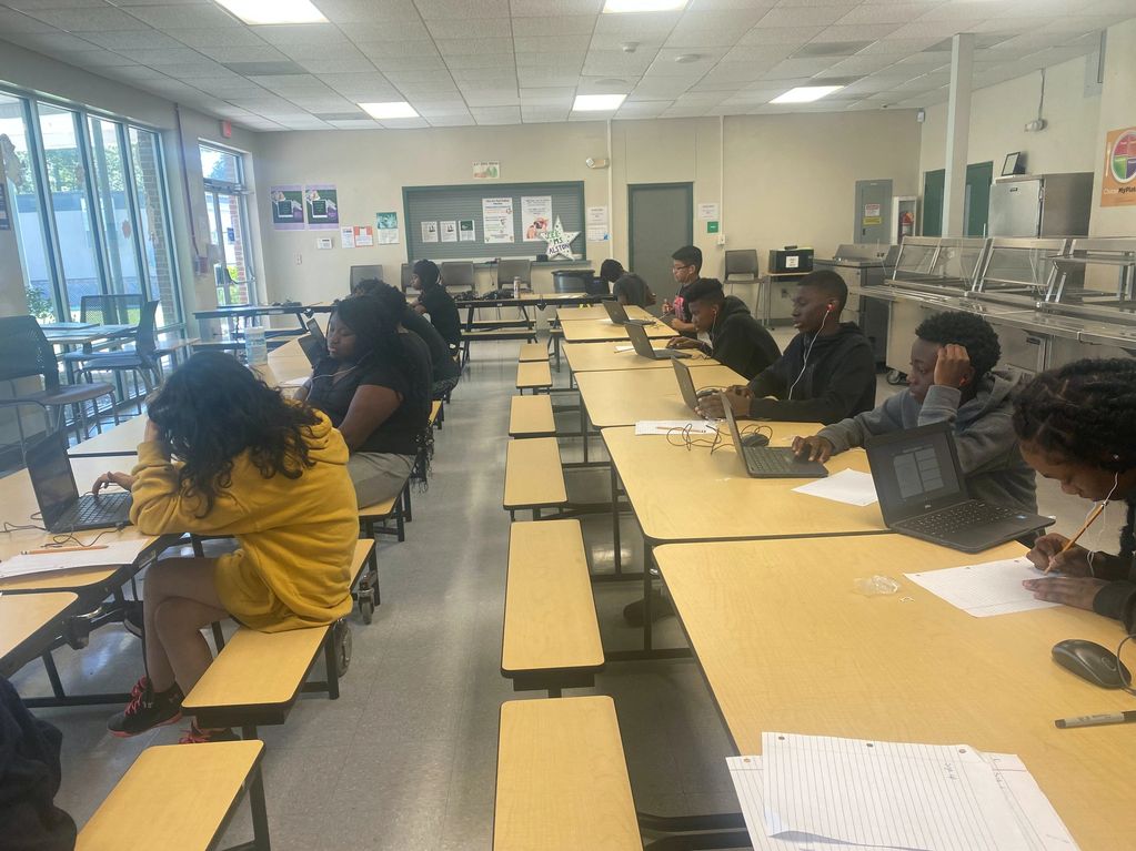 A group of middle school children sit in the lunchroom practicing academics during a Summer Camp.