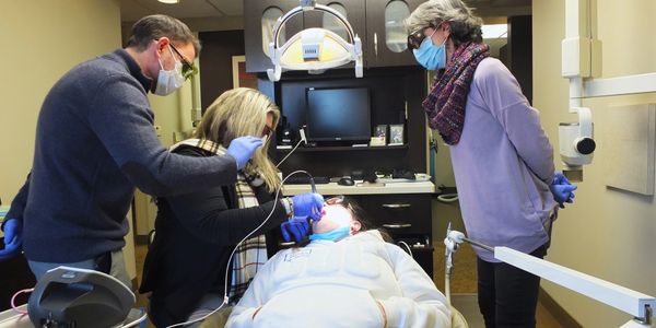 Dentist and assistants treat a patient wearing masks in a clinic.