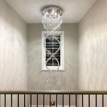 Elegant crystal chandelier spiraling in a narrow stairwell with a window.