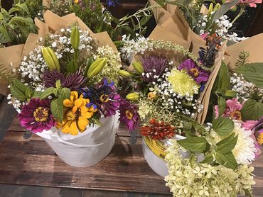 Colorful flower bouquets in white buckets on a wooden table.