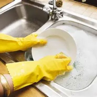 Person washing dishes wearing yellow gloves at a kitchen sink.