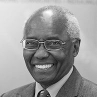 Portrait of an elderly man smiling warmly with glasses and a suit.