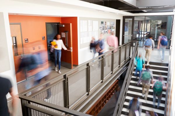 Students moving quickly in a busy school hallway near classrooms and stairs.