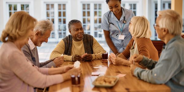 Seniors playing cards with a nurse in a cozy room.