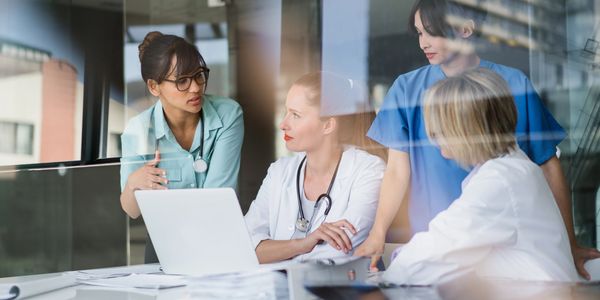 Four medical professionals discussing patient care around a laptop in a modern office.
