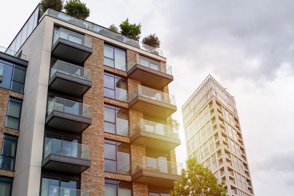 Modern apartment building with glass balconies and rooftop greenery.