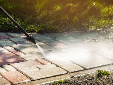 Pressure washer cleaning dirty outdoor pavement blocks near grass and mud.