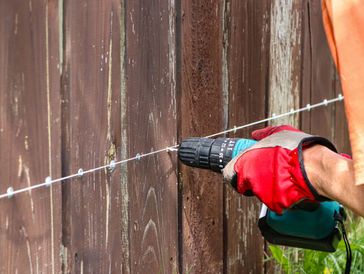 Person drilling into wooden fence with red gloves for outdoor installation