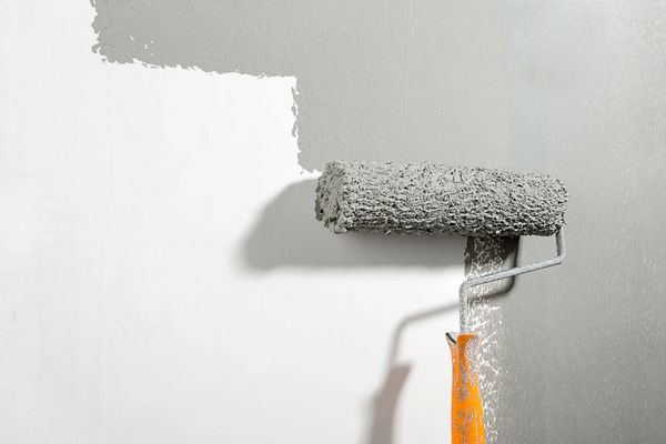 Paint roller applying grey paint on a white wall during home renovation
