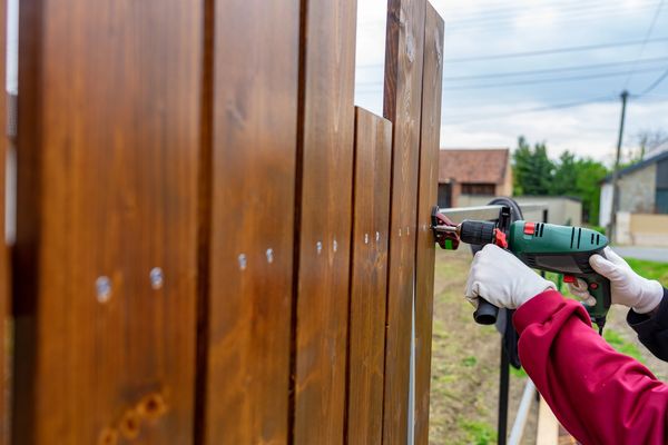 Man building his own special wooden fence with driller.
