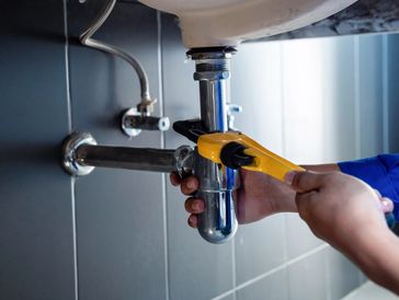 Plumber using wrench to tighten or fix pipe under sink in bathroom or kitchen.