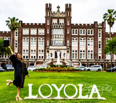 Graduate celebrates in front of Loyola building with large letters on grass.