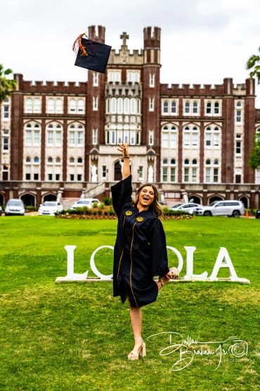 Joyful graduate tossing cap in front of Loyola building.