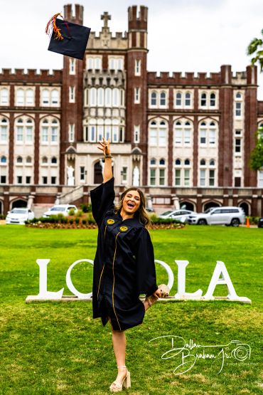 Graduate joyfully tossing cap in front of Loyola building.