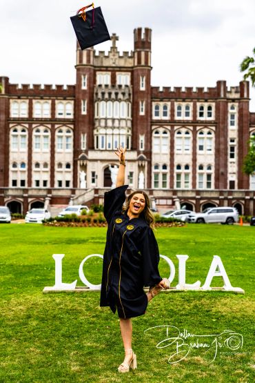 A joyful graduate throws her cap in front of a historic Loyola building.