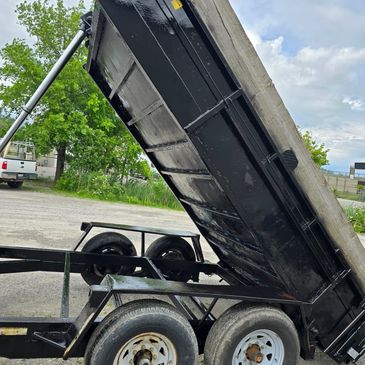 A freshly painted black dump trailer tilted upwards.