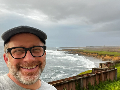 Man smiling near ocean coastline with cloudy sky.
