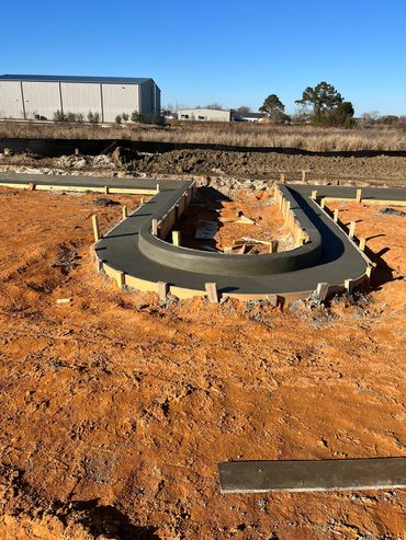 Concrete foundation with wooden forms on a construction site under clear blue sky.