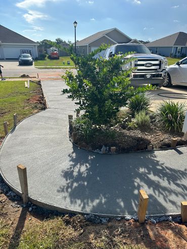 Freshly poured concrete sidewalk curves around a garden in a suburban neighborhood.