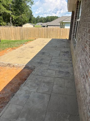Newly poured concrete patio beside a brick house under a sunny sky.