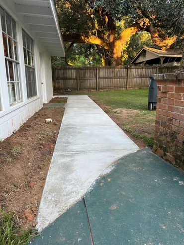 Newly poured concrete walkway beside a house leading to a backyard.