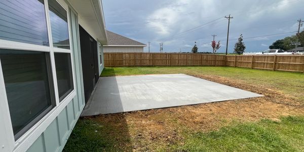 New concrete slab patio in a backyard with a wooden fence.