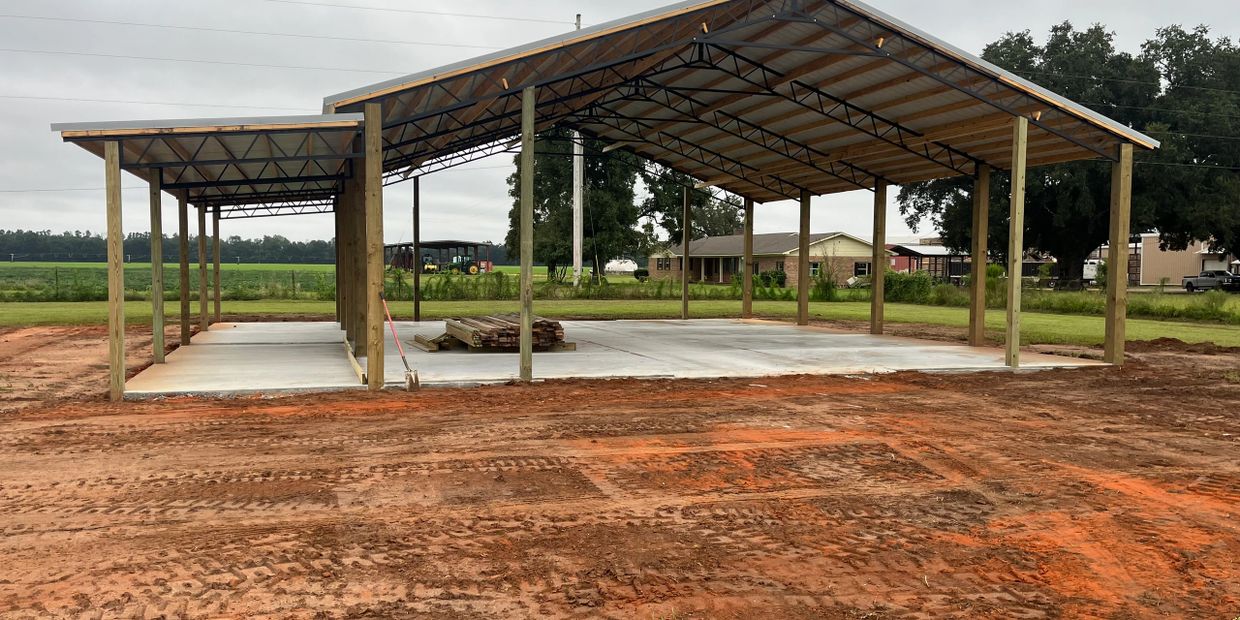 Partially constructed open metal and wood shed on a concrete slab in a rural area.