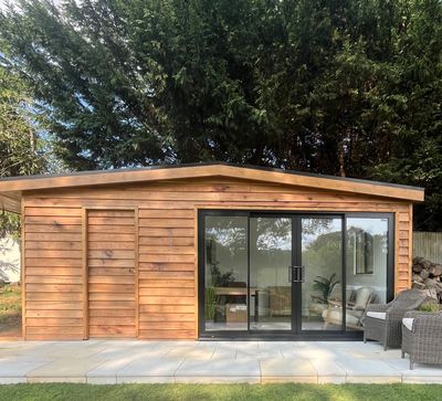 Modern wooden garden room with large glass doors and outdoor seating.