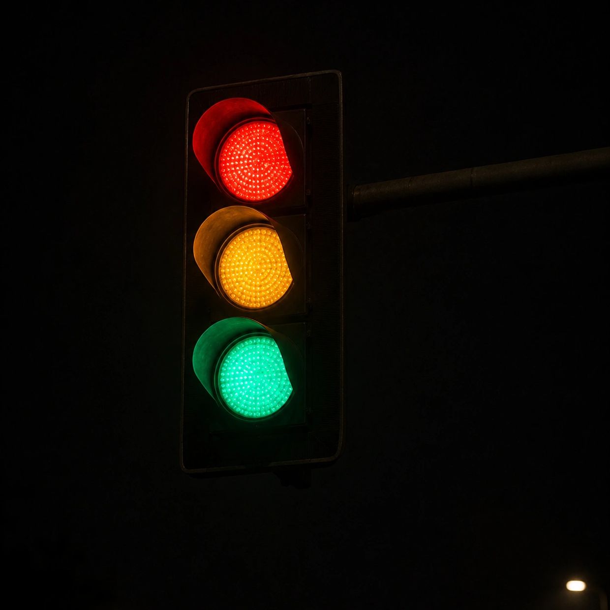 Traffic light showing red, yellow, and green lights at night.
