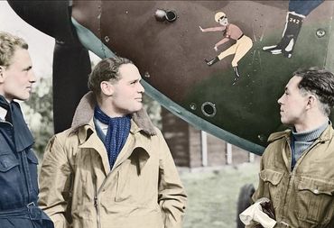 Three World War II pilots stand by a decorated aircraft nose.