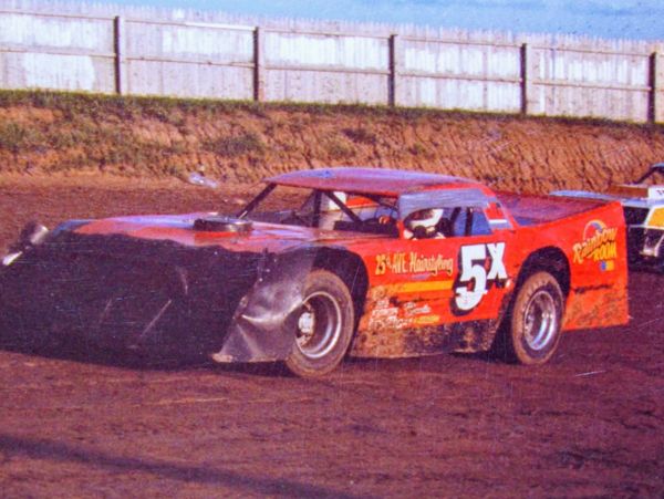 A red dirt track race car with number 5X racing on a dirt track.