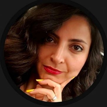 Woman with dark hair and yellow nails posing.