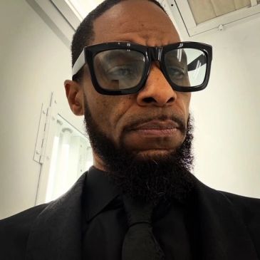Man wearing large black glasses and black tie.