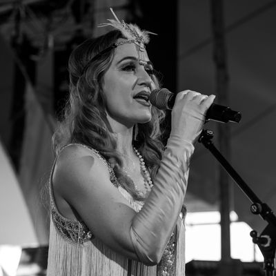 A performer in 1920s attire sings passionately into a microphone on stage.
