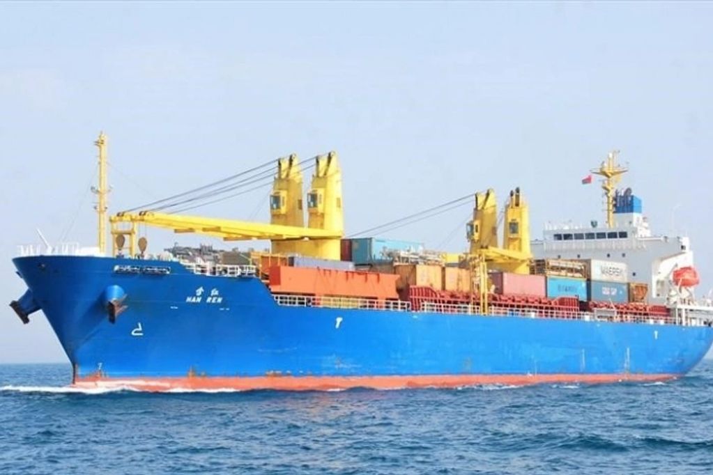 Blue cargo ship with yellow cranes on open sea.