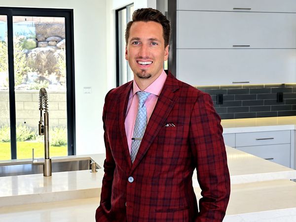 Man wearing a red plaid jacket standing in a modern kitchen.