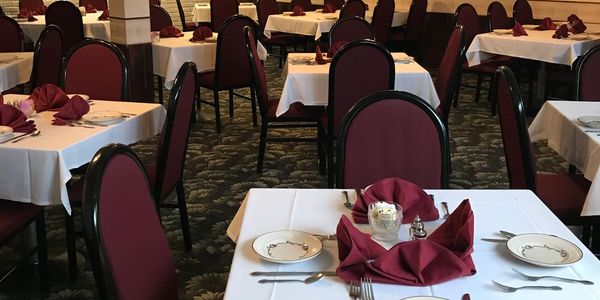 Elegant restaurant tables set with white linens and burgundy napkins.