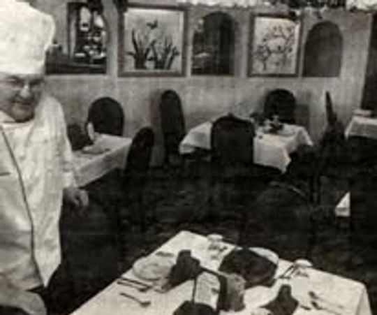 A chef stands beside a table in a vintage restaurant setting.