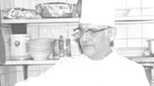A chef in a white uniform and hat in a kitchen.