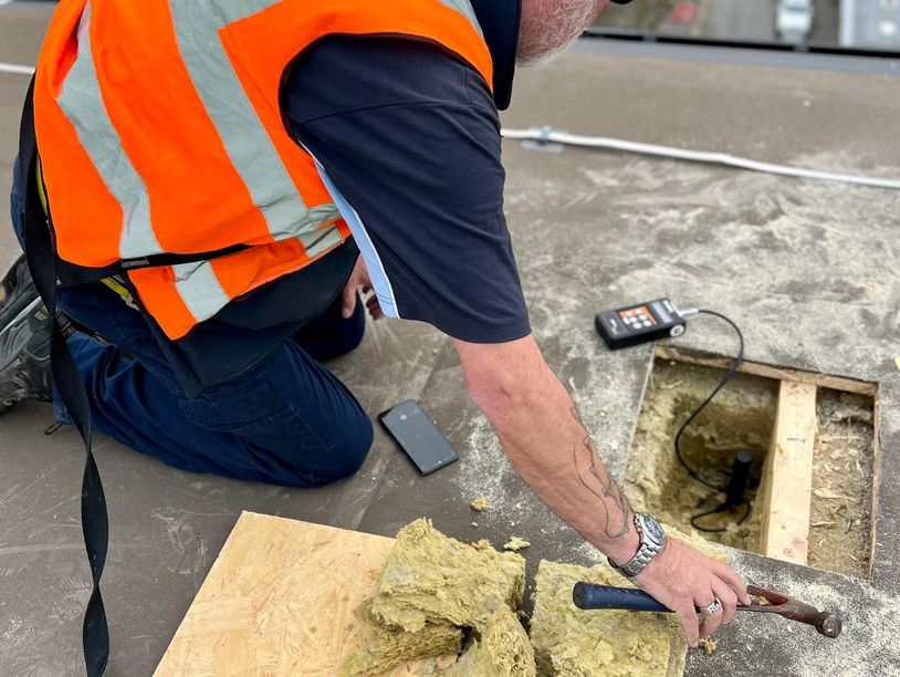 Worker in orange vest repairing roof insulation with tools and equipment.
