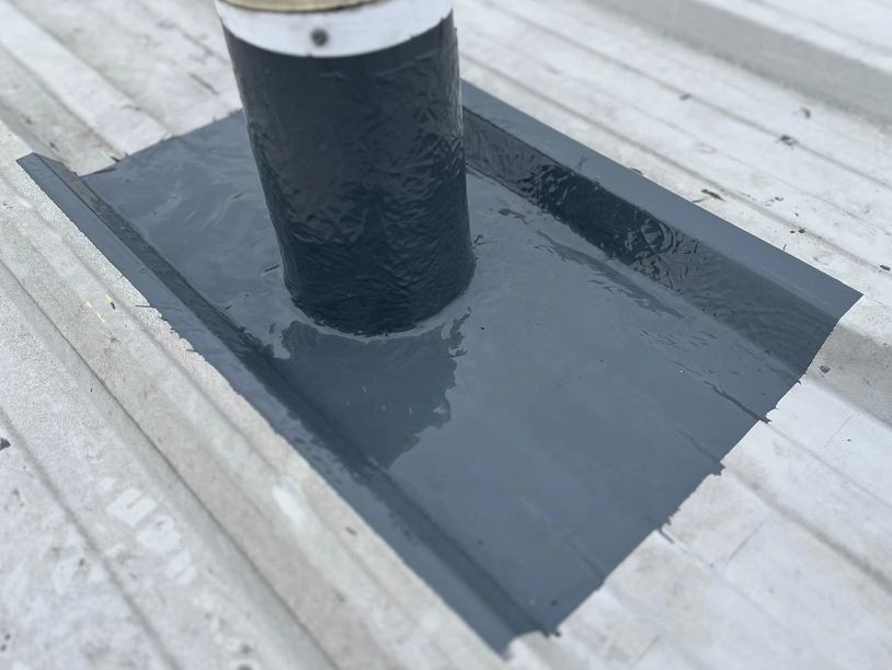 Black waterproof sealant applied around a pipe on a corrugated metal roof.