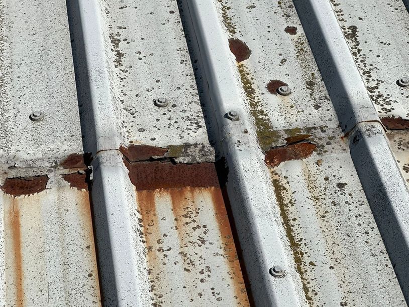 Rusty and damaged corrugated metal roof panels with visible screws.
